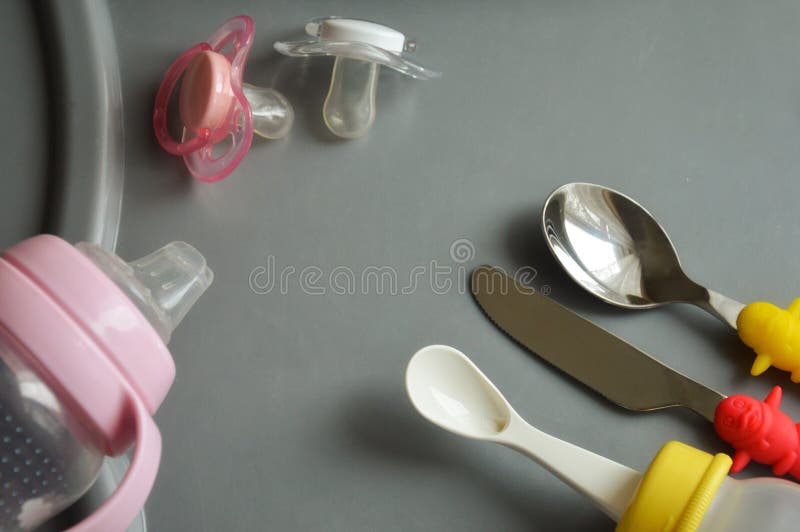 Artículos para alimentar al bebé botellas, entrerroscas, cucharas y un cuchillo en la tabla gris imagen de archivo Artículos para alimentar al bebé botellas, entrerroscas, cucharas y un cuchillo en la tabla gris imagen de archivo