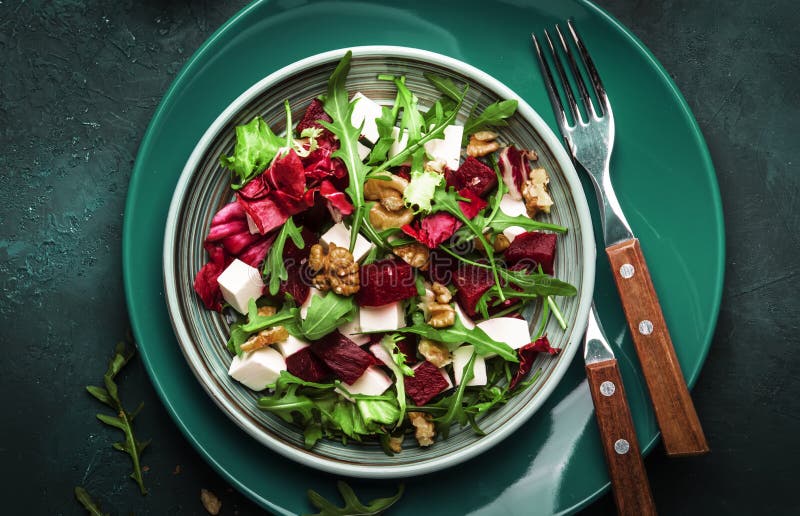 Arugula, Beet and cheese salad with fresh radicchio and walnuts on plate with fork, dressing and spices on blue kitchen table