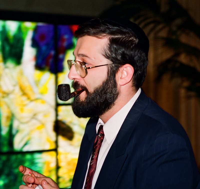 Shas Party leader Aryeh Deri participates in the installation of the new Labor Party government, led by Yitzhak Rabin on July 14, 1992 at the President`s residence, Beit Hanassi.  By this time, Deri had taken up smoking a pipe and would join the government in a show of unity.  In 1999 he was convicted of fraud, bribery, and breech of trust, and served 2 years in prison.  In 2013 he ran again and won.  In 2022, he was convicted of tax crimes.  The Israel Supreme Court said this disqualified him for a seat in the Netanyahu government in January, 2023.  His fate remains uncertain.  Shas is Sephardic Orthodox religious party with a large working class constituency of Moroccan Jewish descent. The artist of the colorful stained glass in the background of Ceremonial Hall of Beit Hanassi is Reuven Rubin. Shas Party leader Aryeh Deri participates in the installation of the new Labor Party government, led by Yitzhak Rabin on July 14, 1992 at the President`s residence, Beit Hanassi.  By this time, Deri had taken up smoking a pipe and would join the government in a show of unity.  In 1999 he was convicted of fraud, bribery, and breech of trust, and served 2 years in prison.  In 2013 he ran again and won.  In 2022, he was convicted of tax crimes.  The Israel Supreme Court said this disqualified him for a seat in the Netanyahu government in January, 2023.  His fate remains uncertain.  Shas is Sephardic Orthodox religious party with a large working class constituency of Moroccan Jewish descent. The artist of the colorful stained glass in the background of Ceremonial Hall of Beit Hanassi is Reuven Rubin.