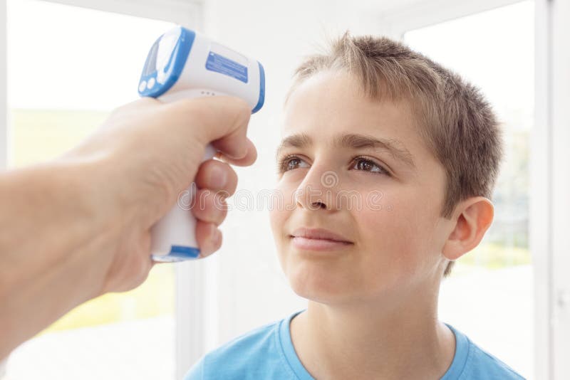 Doctor or teacher checks boy`s body temperature using infrared forehead thermometer for symptoms of Coronavirus or other infections. Doctor or teacher checks boy`s body temperature using infrared forehead thermometer for symptoms of Coronavirus or other infections