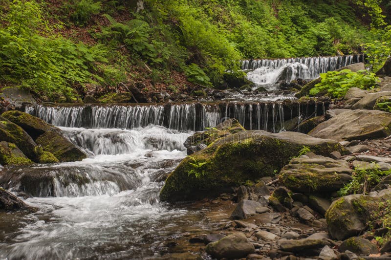 As cascatas da montanha fluem a água do rolamento nas rochas imagem de stock As cascatas da montanha fluem a água do rolamento nas rochas imagem de stock