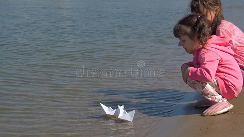 As crianças deixaram os barcos ir Meninas no rio com barcos de papel Duas irmãs estão jogando pela água