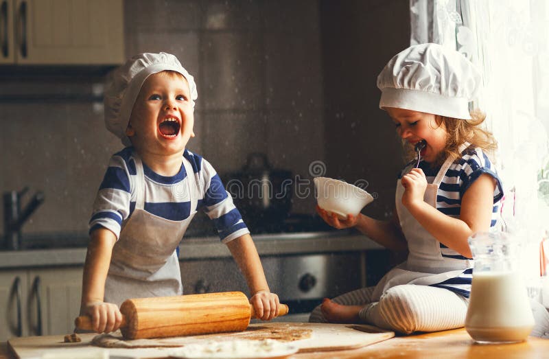 As crianças engraçadas da família feliz cozem cookies na cozinha