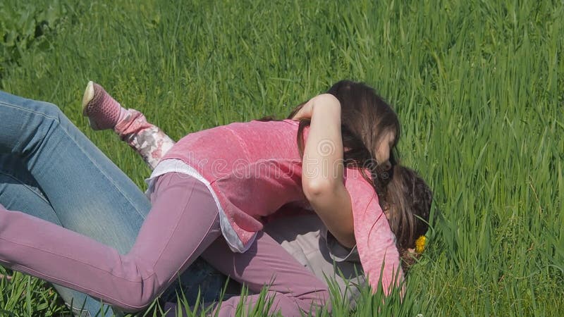 As crianças estão abraçando a mamã no parque As meninas deixam cair a mãe na grama verde Família no parque em uma tarde ensolarad