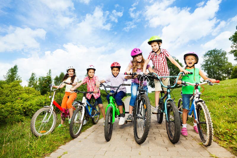 As crianças felizes na fileira vestem capacetes coloridos da bicicleta