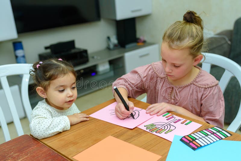 Needlework, crafts children.Little girl create a greeting card image of the Jewish holiday of Hanukkah.Kidd pastes stickers, glue candles and drawing menorah, dreidel, oil jar on paper on wooden table. Needlework, crafts children.Little girl create a greeting card image of the Jewish holiday of Hanukkah.Kidd pastes stickers, glue candles and drawing menorah, dreidel, oil jar on paper on wooden table