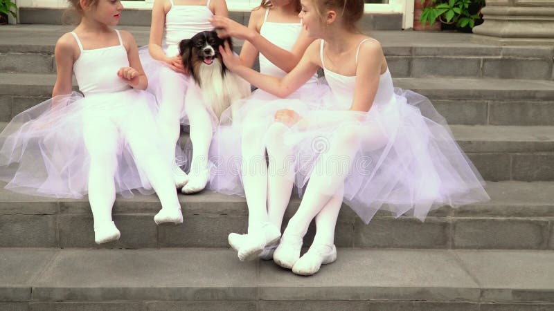 As estudantes pequenas da escola do bailado sentam-se em um patamar da escola As bailarinas pequenas sentam-se em um patamar na e