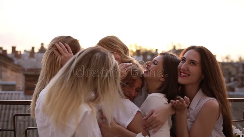 As meninas caucasianos atrativas estão abraçando a parte externa ereta em um terraço ou em um balcão Seis jovens mulheres bonitas