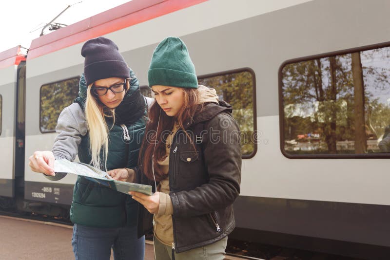 As moças do moderno com trouxa e mapa esperam o trem Mulheres que viajam apenas no estação de caminhos-de-ferro, conceito do curs fotos de stock As moças do moderno com trouxa e mapa esperam o trem Mulheres que viajam apenas no estação de caminhos-de-ferro, conceito do curs fotos de stock