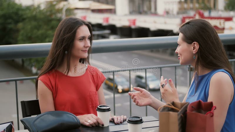 As mulheres bonitas que bebem o café comunicam-se em um café com uma ideia do tráfego, falando após a compra 4K