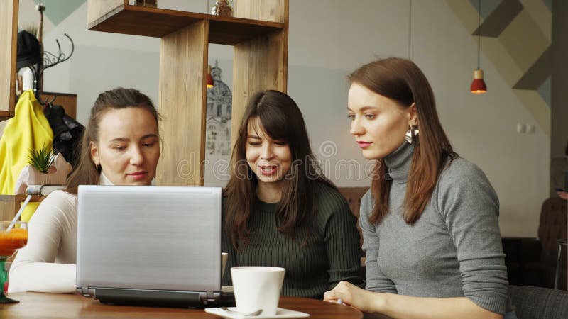 As mulheres dos colegas discutem o projeto comum no café usando um portátil