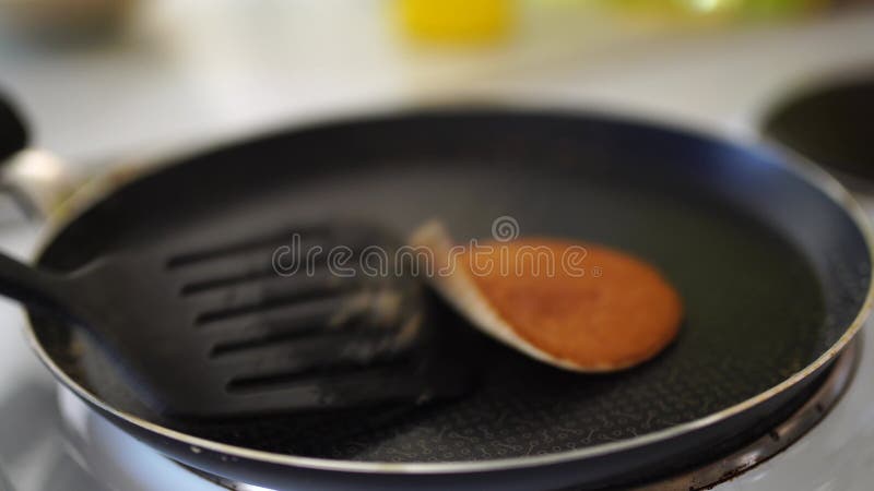 As mãos das meninas em um avental azul são removidas da panqueca com uma espátula. coloca as panquecas em uma pilha.