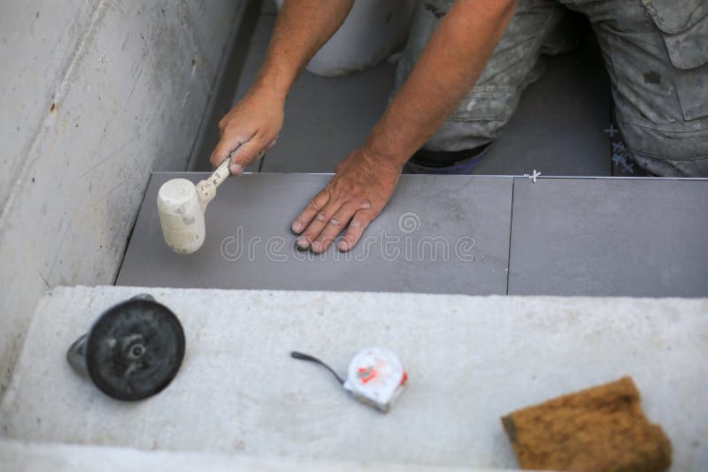 As mãos do cilindro estão colocando o azulejo cerâmico no chão imagem de stock As mãos do cilindro estão colocando o azulejo cerâmico no chão imagem de stock