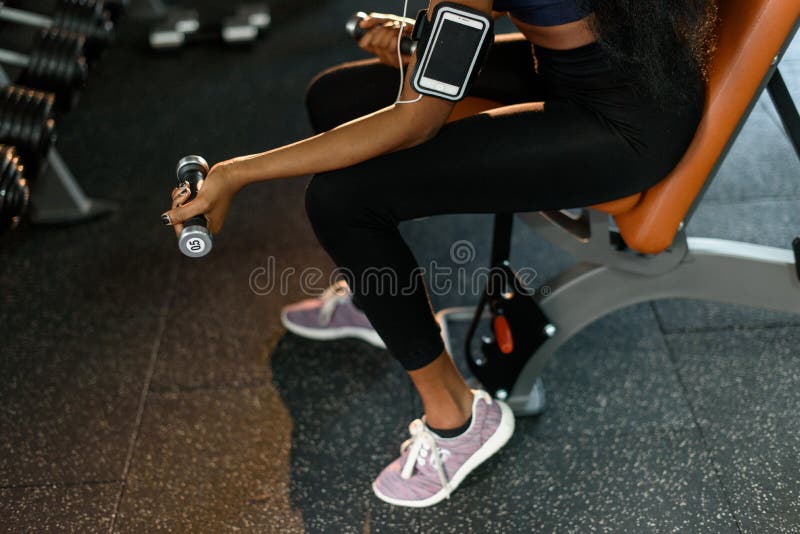 As mãos do close-up da mulher afro-americano da aptidão 'sexy' que dá certo com pesos no gym e escutam música dentro fotos de stock royalty free As mãos do close-up da mulher afro-americano da aptidão 'sexy' que dá certo com pesos no gym e escutam música dentro fotos de stock royalty free