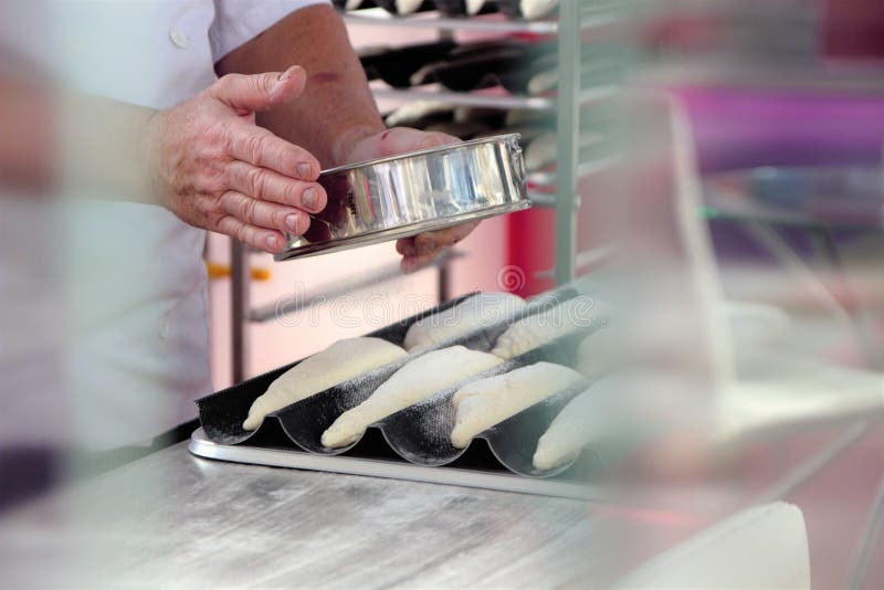 As mãos do padeiro polvilham a farinha de cozimento, antes de fazê-la no forno imagem de stock As mãos do padeiro polvilham a farinha de cozimento, antes de fazê-la no forno imagem de stock