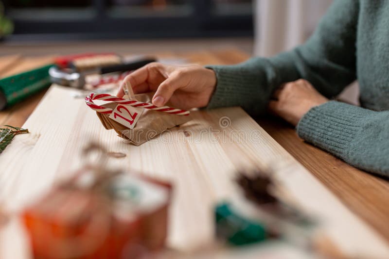 winter holidays and hobby concept - hands with clothespin, craft paper bag and candy cane making advent calendar on christmas at home. winter holidays and hobby concept - hands with clothespin, craft paper bag and candy cane making advent calendar on christmas at home