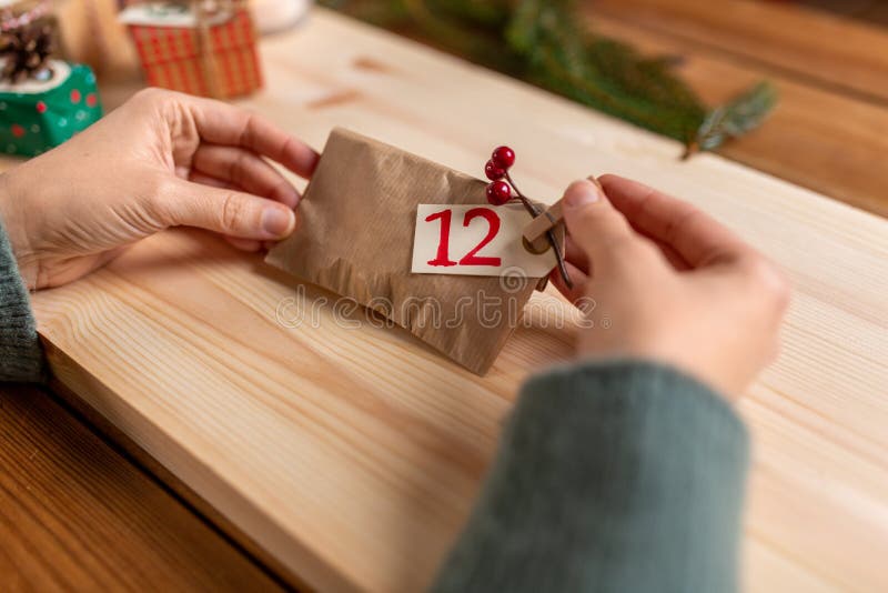 winter holidays and hobby concept - hands with clothespin, craft paper bag and tag making advent calendar on christmas at home. winter holidays and hobby concept - hands with clothespin, craft paper bag and tag making advent calendar on christmas at home