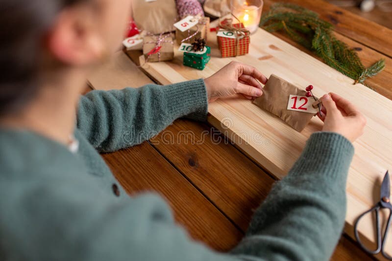 winter holidays and hobby concept - hands with clothespin, craft paper bag and tag making advent calendar on christmas at home. winter holidays and hobby concept - hands with clothespin, craft paper bag and tag making advent calendar on christmas at home