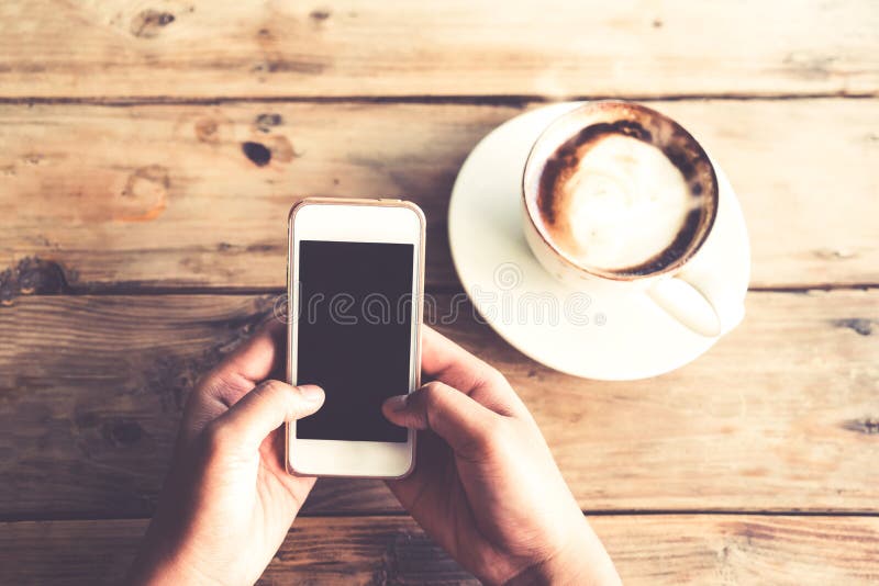 as mãos novas bonitas do ` s da mulher do moderno que guardam o telefone esperto móvel com o copo de café quente no café compram fotografia de stock royalty free as mãos novas bonitas do ` s da mulher do moderno que guardam o telefone esperto móvel com o copo de café quente no café compram fotografia de stock royalty free