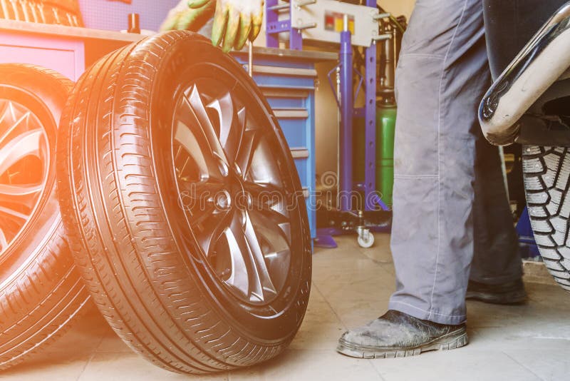 As rodas de mudanças do trabalhador do mecânico no carro na garagem do serviço de reparação de automóveis compram fotografia de stock As rodas de mudanças do trabalhador do mecânico no carro na garagem do serviço de reparação de automóveis compram fotografia de stock
