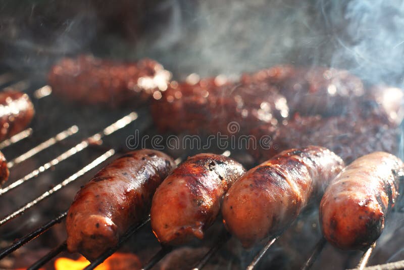 As salsichas no assado grelham com fumo e flama fotografia de stock As salsichas no assado grelham com fumo e flama fotografia de stock