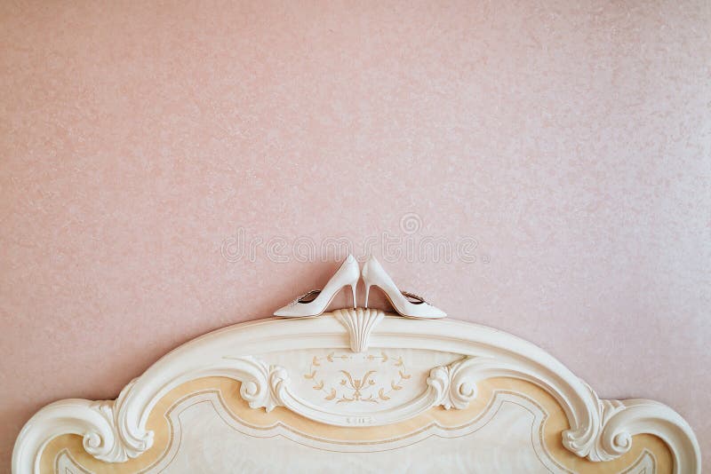 As sapatas do ` s das mulheres do casamento do marfim estão no bedhead perto da parede fotografia de stock royalty free As sapatas do ` s das mulheres do casamento do marfim estão no bedhead perto da parede fotografia de stock royalty free