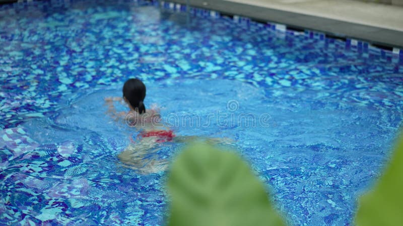 in and out of focus footage of Asia Chinese woman swimming away from view in private pool