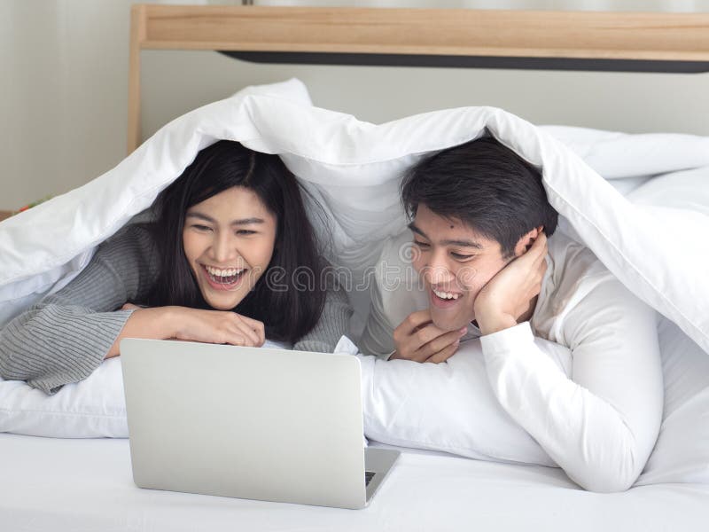 Asian Adorable Young Couple Lying Under Blanket On Their Bed Enjoy