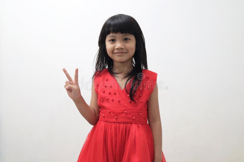 Asian baby girl wearing red dress showing victory hand sign or number two with her fingers, looking at camera and smiling happy royalty free stock photos