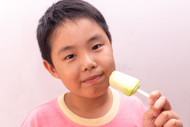 Asian boy eating a colorful frozen popsicle in the summer.