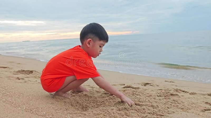 Asian boy playing in the sand at the beach. stock video footage