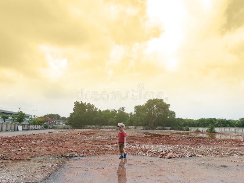 Asian boy stand alone in the demolition wasteland construction area at the sunset time with raylight and cloudy.