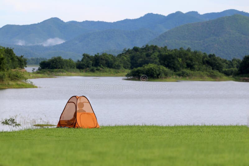 Asian Buddist people are prays meditations in the mesh dome or tents on the lawn with beautiful landscapes of dam water, forests, and mountains in Thailand