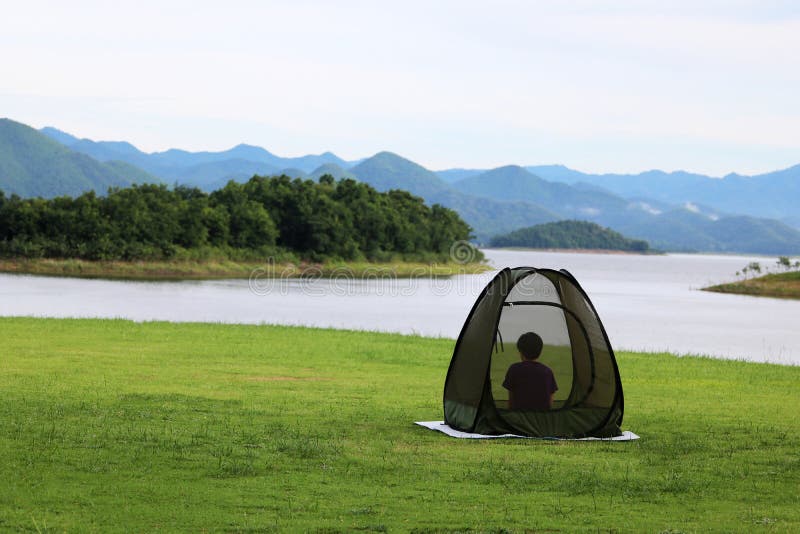 Asian Buddist people are prays meditations in the mesh dome or tents on the lawn with beautiful landscapes of dam water, forests, and mountains in Thailand