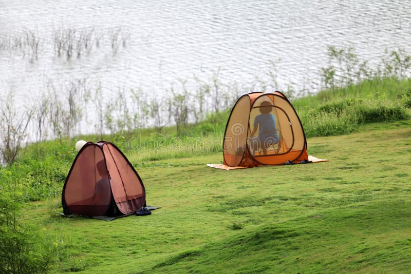 Asian Buddist people are prays meditations in the mesh dome or tents on the lawn with beautiful landscapes of dam water, forests, and mountains in Thailand.