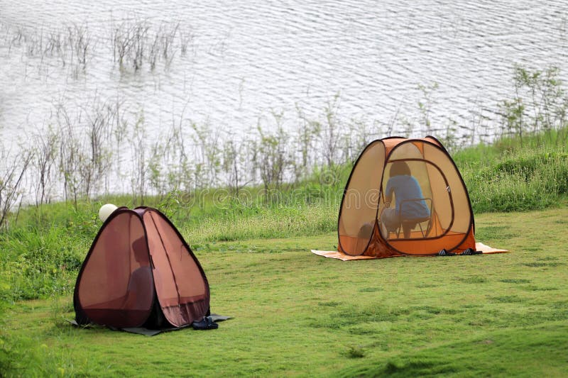 Asian Buddist people are prays meditations in the mesh dome or tents on the lawn with beautiful landscapes of dam water, forests, and mountains in Thailand.