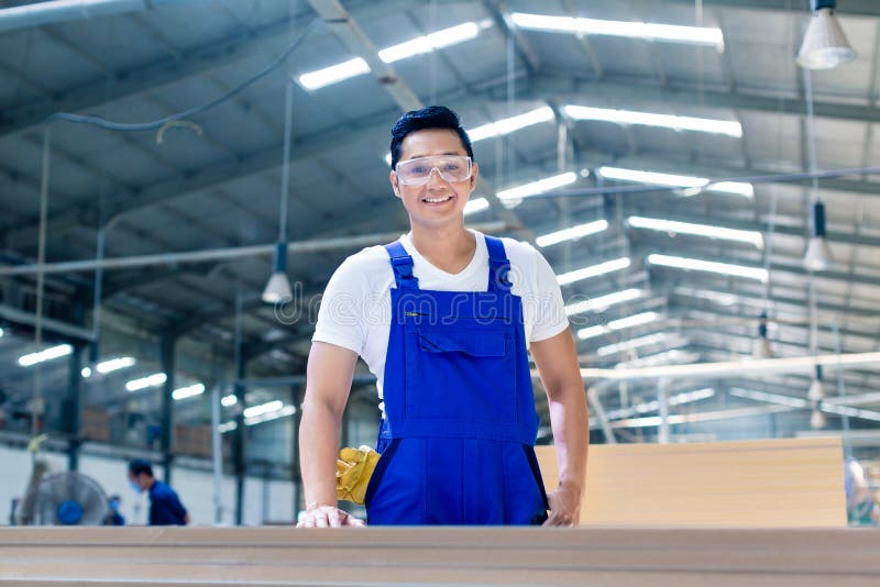 Asian carpenter standing in workshop with wood boards