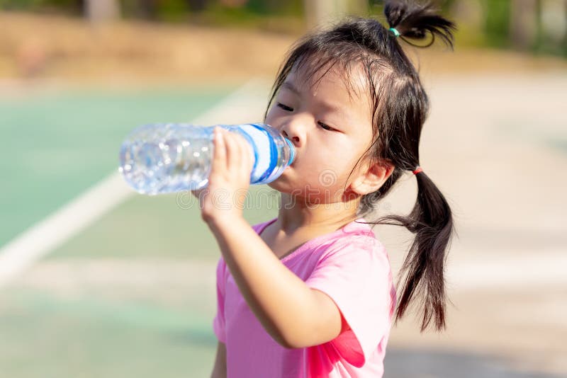 Asian child are drinking some water from plastic bottles. Cute girl thirsty. Hot summer or spring. Children sweats on the face.