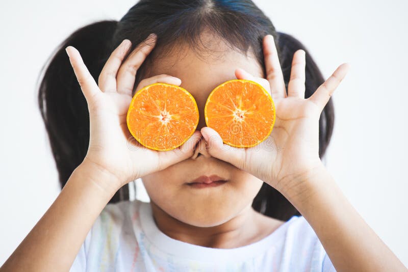 Asian child girl holding fresh oranges covering her eyes. Kid having fun to play with fresh fruit