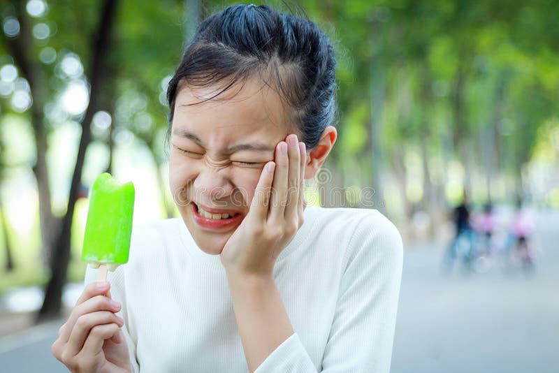 Asian child girl holding her hand on her aching tooth have hypersensitive teeth eating ice-cream,feel painful,female teenage have