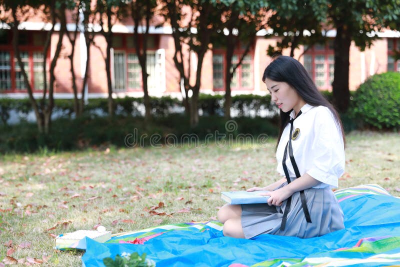 Happy Asian Chinese pretty girl wear student suit in school read book sit on grass