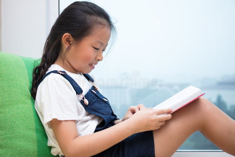 Asian Chinese little girl reading book on the windowsill
