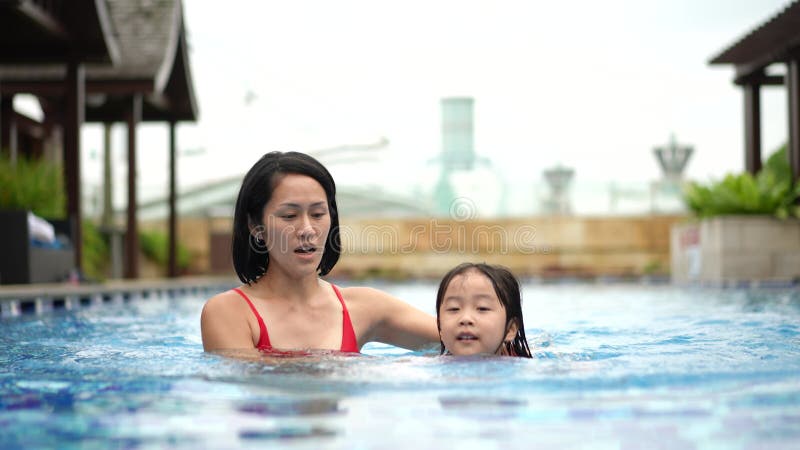 Asian Chinese mother and daughter learning how to swim at the pool frontal view