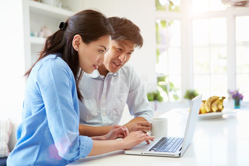 Asian Couple Looking at Laptop In Kitchen