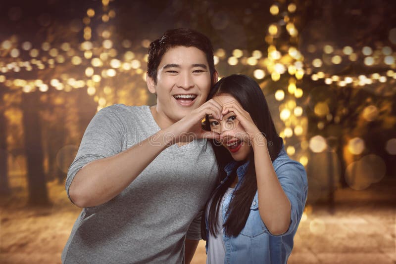 Asian couple standing close to each other and looking through a stock photo.