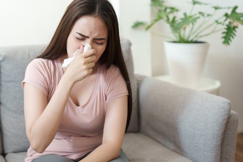 Asian Cute of  girl having  flu season and sneeze using paper tissues sitting on sofa at home, Health and illness concepts