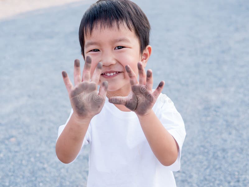 Asian cute little child boy showing dirty black hands while playing outdoor. Happy kid enjoy in relaxing day