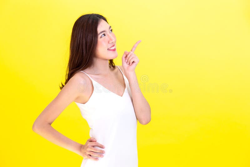 Asian cute woman pointing hands to empty copy space and posing arms akimbo isolated on yellow background