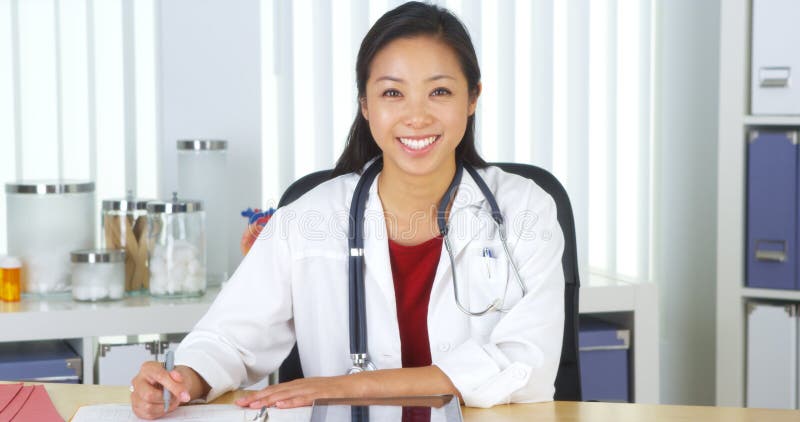Asian doctor smiling to camera at desk
