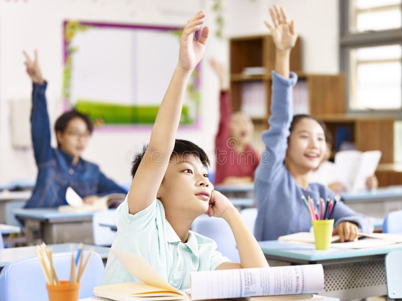 Asian elementary school students raising hands in class